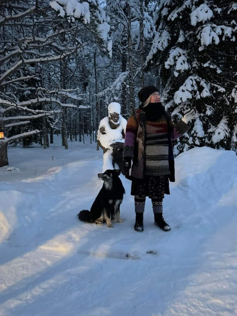 En kvinne og en hun står foran en statue i en snødekket barskog.
