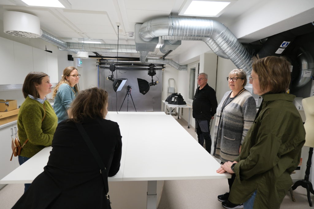 Seks personer står rundt et hvitt bord i et rom med fotoutstyr i bakgrunnen.